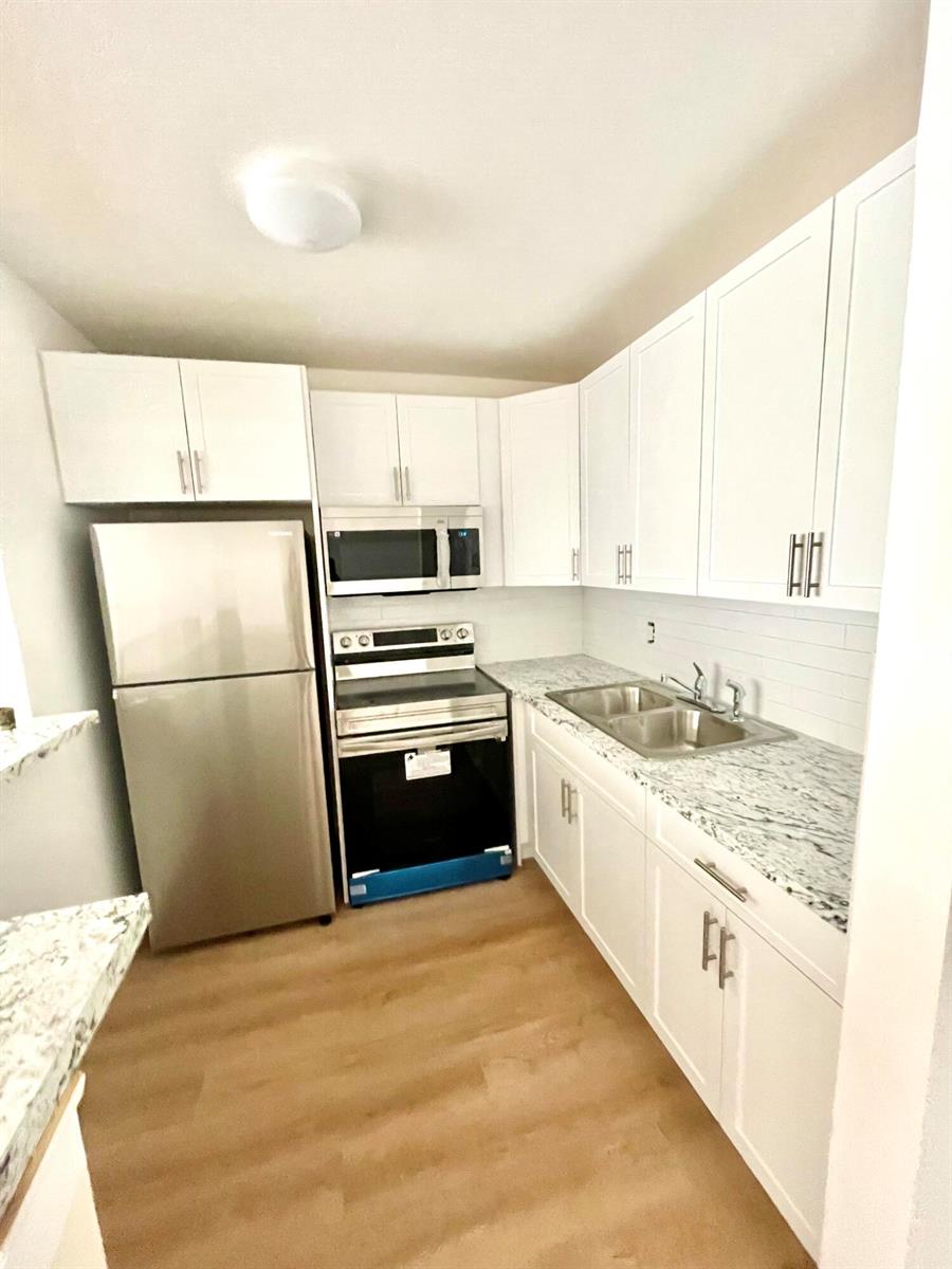 A kitchen features white cabinets, stainless steel appliances, and granite countertops over light wood flooring — 203 Easthampton I, West Palm Beach FL 33417, WEST PALM BEACH, FL