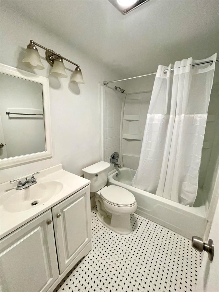 A bathroom features a white vanity, a toilet, and a shower-tub combo with white tile — 203 Easthampton I, West Palm Beach FL 33417, WEST PALM BEACH, FL