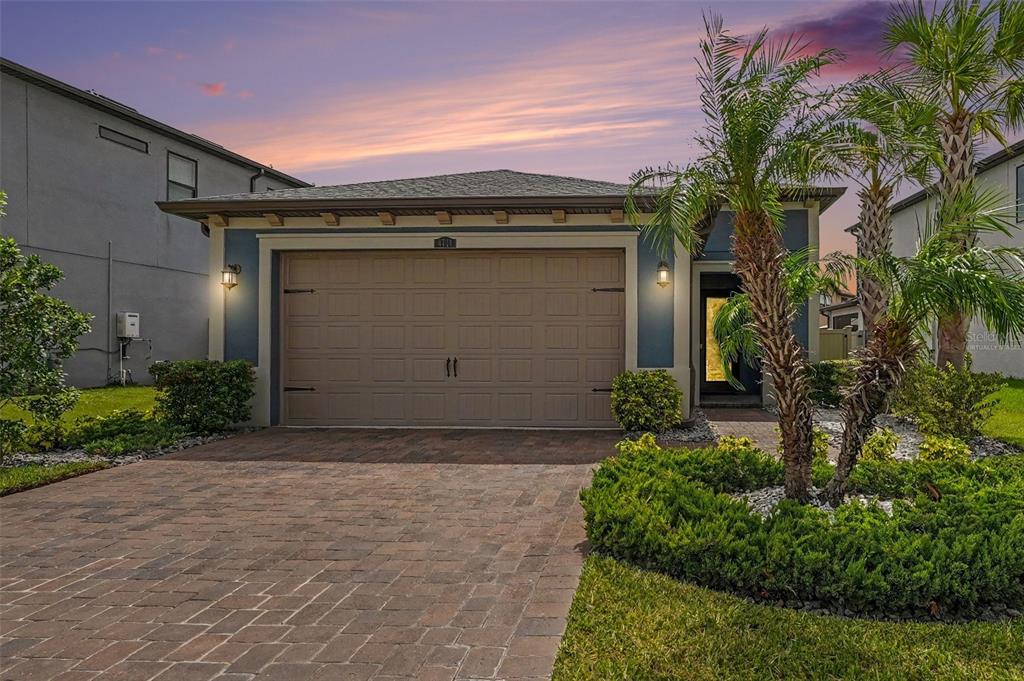 A single-story house with a tan garage door and a paved driveway at sunset — 4711 SAN MARTINO DRIVE, WESLEY CHAPEL, FL