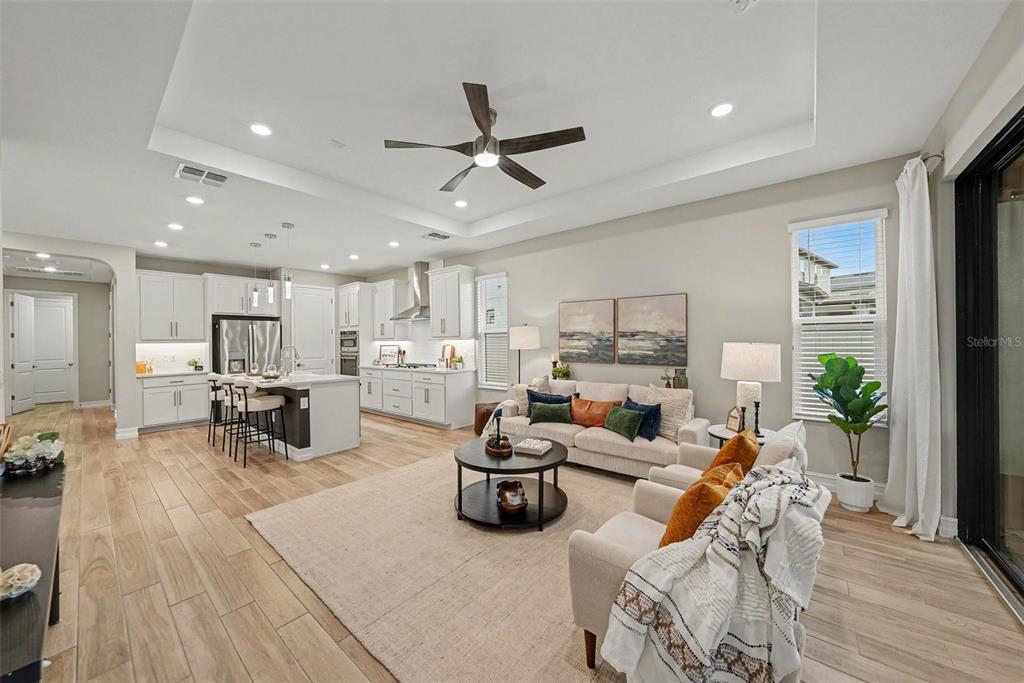 An open-concept living room and kitchen featuring white cabinetry, light wood floors, and recessed lighting — 4711 SAN MARTINO DRIVE, WESLEY CHAPEL, FL