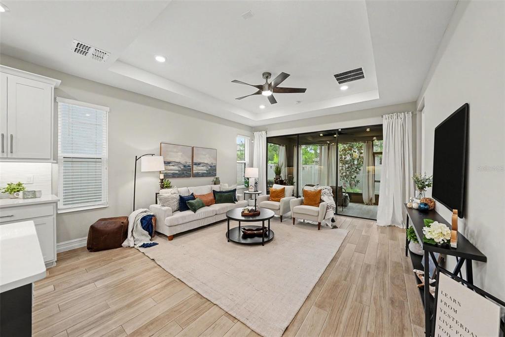 A living room features a tray ceiling, light wood-look flooring, and a large sliding glass door — 4711 SAN MARTINO DRIVE, WESLEY CHAPEL, FL