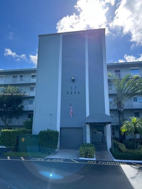 A multi-story apartment building exterior features a blue facade, a covered entrance, and landscaping — 2226 N Cypress Bend Dr # 210, Pompano Beach FL 33069, POMPANO BEACH, FL