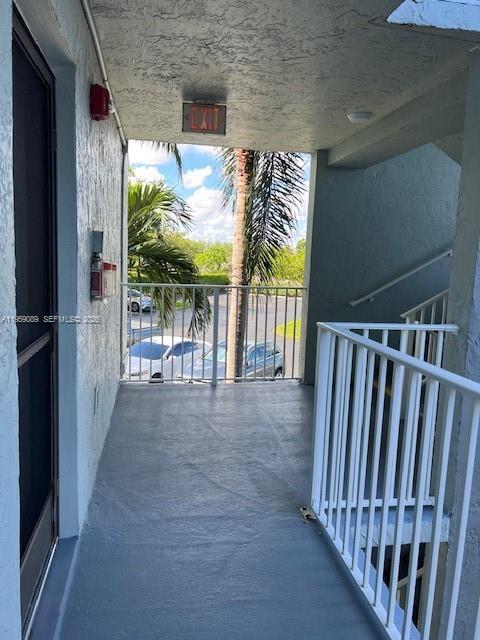 A covered outdoor walkway with a painted concrete floor, white railings, and an exit sign — 2226 N Cypress Bend Dr # 210, Pompano Beach FL 33069, POMPANO BEACH, FL