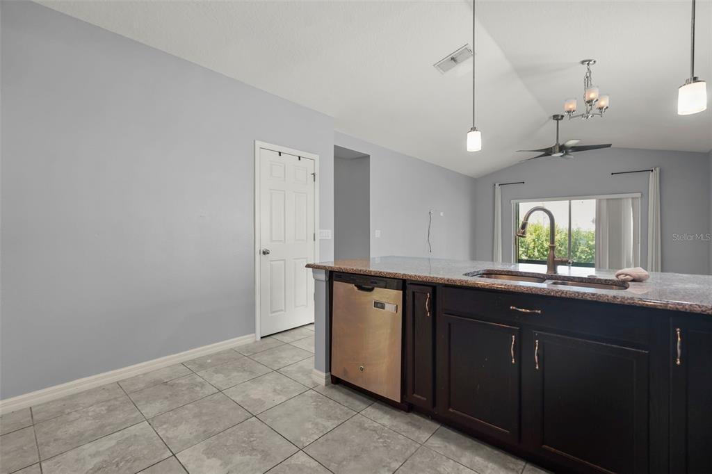 A kitchen features dark wood cabinets, a granite countertop, a dishwasher, and tile flooring — 1300 CAVENDER CREEK RD, MINNEOLA, FL