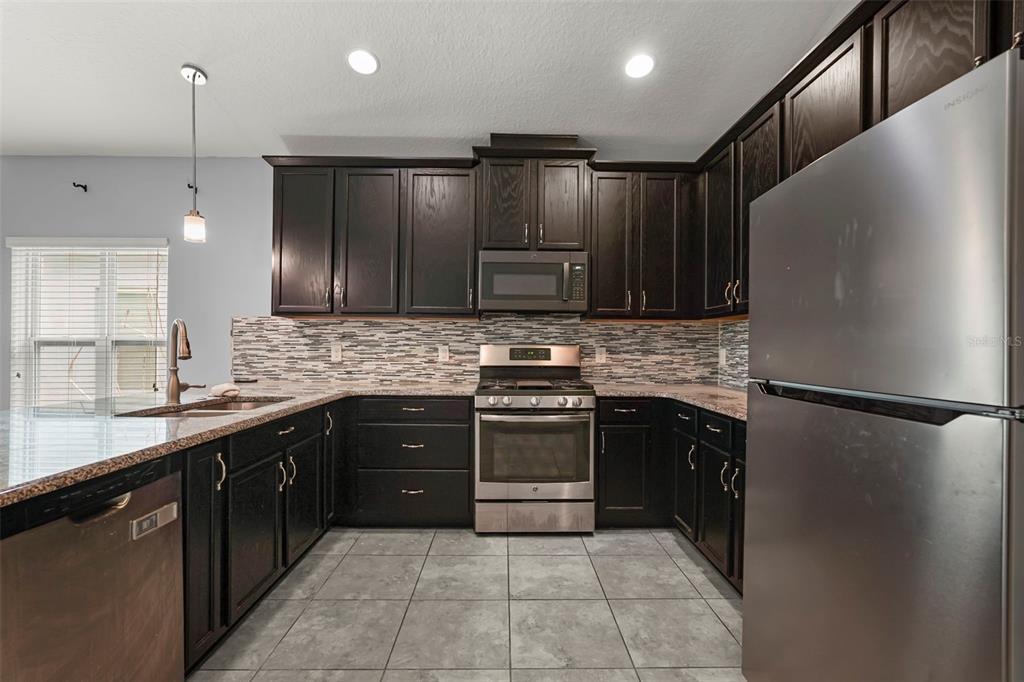 A kitchen features dark wood cabinets, stainless steel appliances, granite countertops, and a tiled floor — 1300 CAVENDER CREEK RD, MINNEOLA, FL