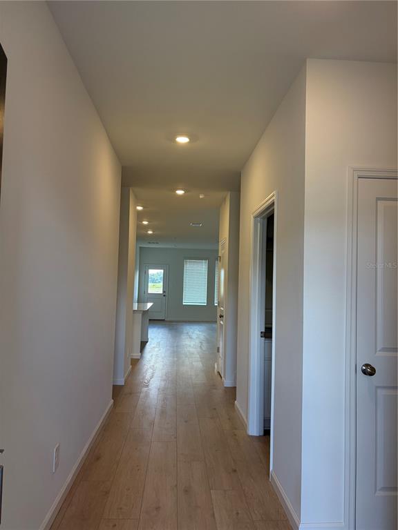 A hallway with light wood-look flooring leads toward an open living area with windows — 4389 VIBERNUM AVENUE, ST CLOUD, FL