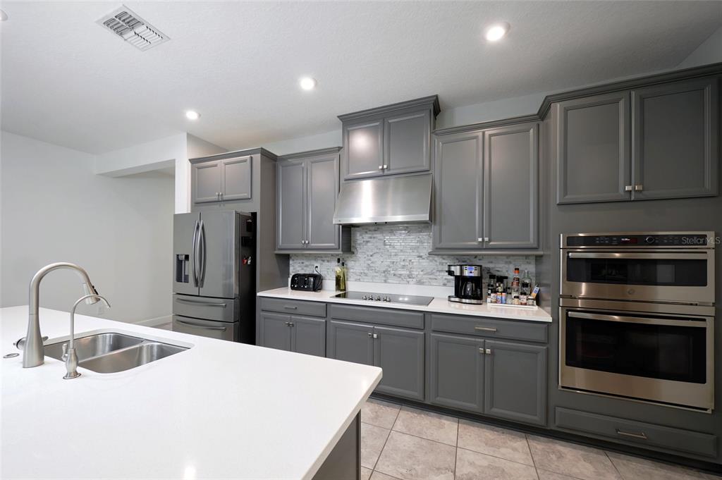 A modern kitchen features gray cabinets, stainless steel appliances, and a white quartz island countertop — 3081 AGOSTINO TERRACE, KISSIMMEE, FL