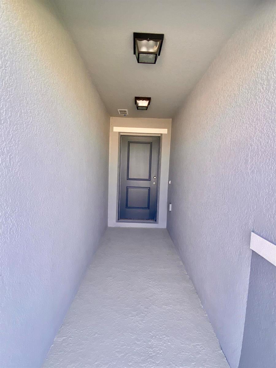 A narrow, covered entryway features light gray walls, a concrete floor, and two ceiling lights — 2460 Begonia Street, FL 34753, FL