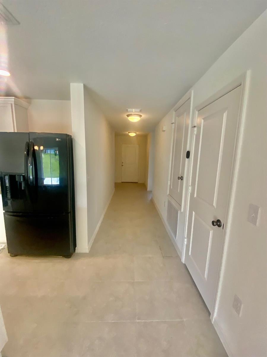 A hallway with tile flooring leads past a black refrigerator and white doors — 2460 Begonia Street, FL 34753, FL
