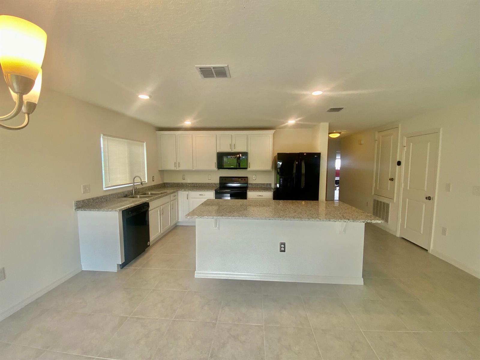 A kitchen with white cabinets, granite countertops, black appliances, and a central island — 2460 Begonia Street, FL 34753, FL