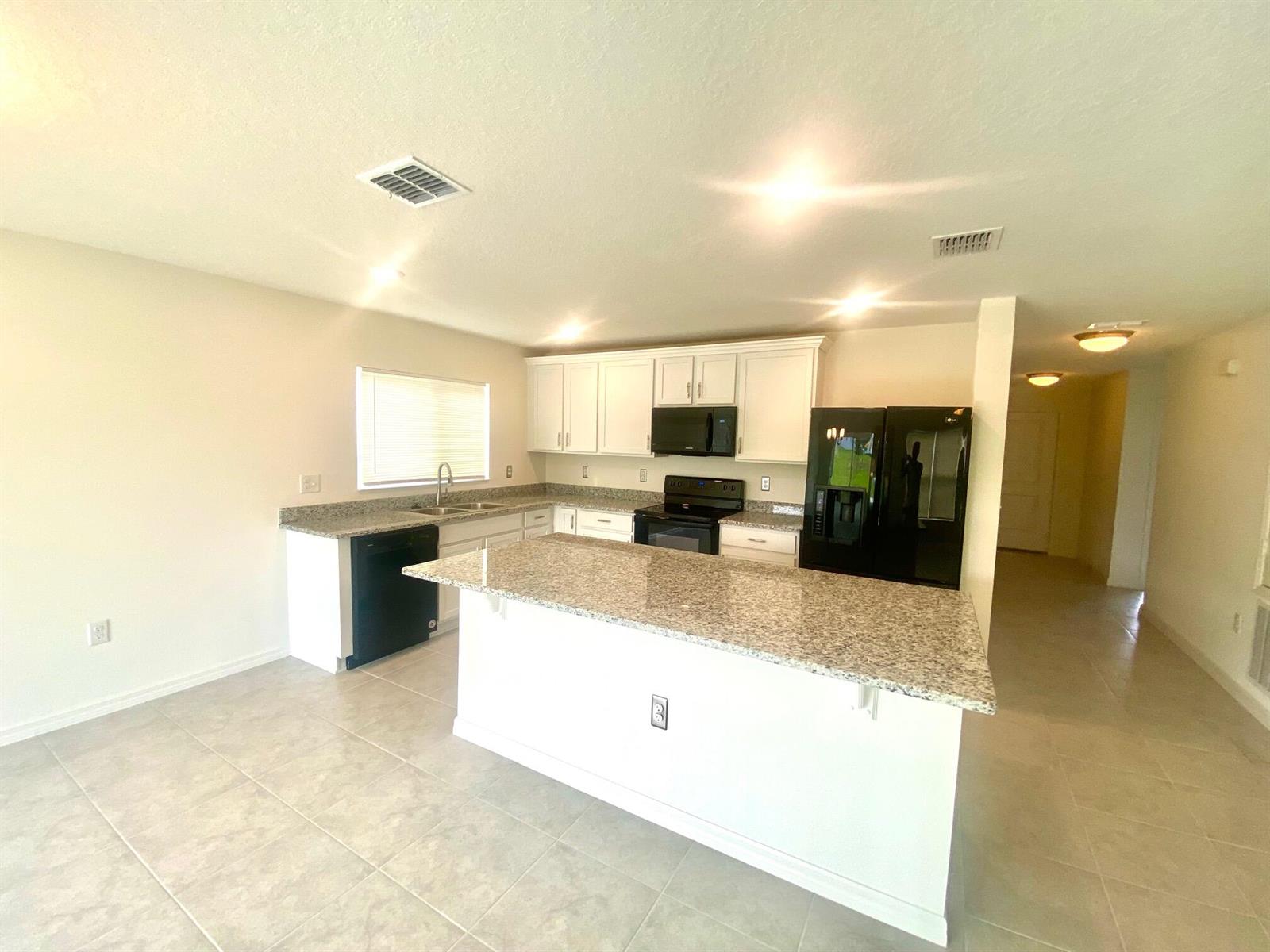 A kitchen with white cabinets, granite countertops, an island, and black appliances — 2460 Begonia Street, FL 34753, FL