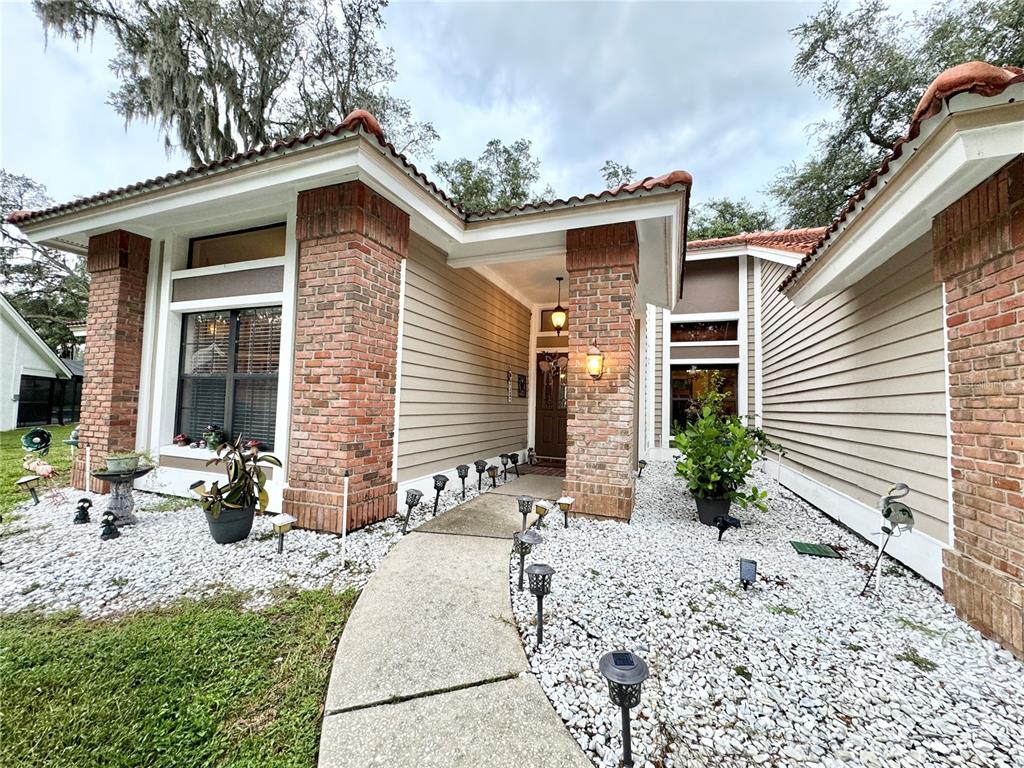 The exterior of a house features brick columns, tan siding, a tiled roof, and a stone walkway — 5455 PINE BARK LANE, WESLEY CHAPEL, FL