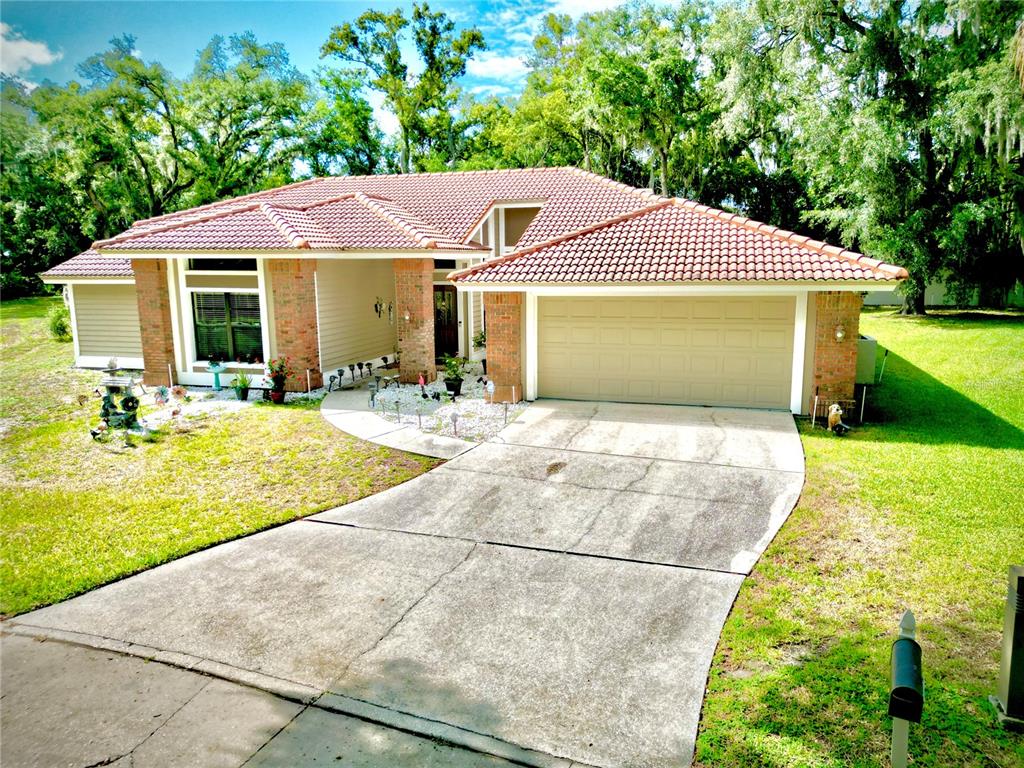 A single-story house with a tiled roof, brick accents, and a concrete driveway — 5455 PINE BARK LANE, WESLEY CHAPEL, FL