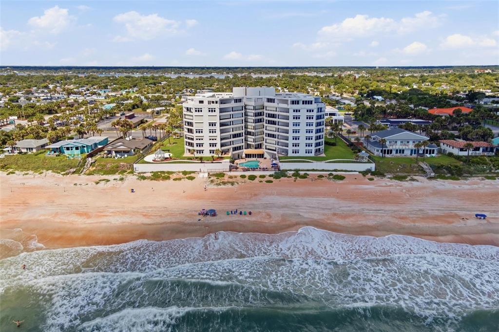 An aerial view shows a multi-story beachfront condominium building with a pool and sandy beach — 395 S ATLANTIC AVENUE UNIT 402, ORMOND BEACH, FL