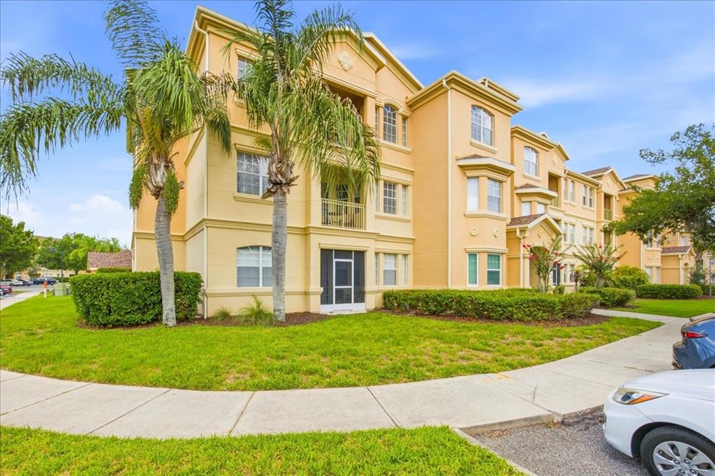 A three-story tan apartment building with palm trees and a sidewalk in the foreground — 301 TERRACE RIDGE CIRCLE UNIT 301, DAVENPORT, FL