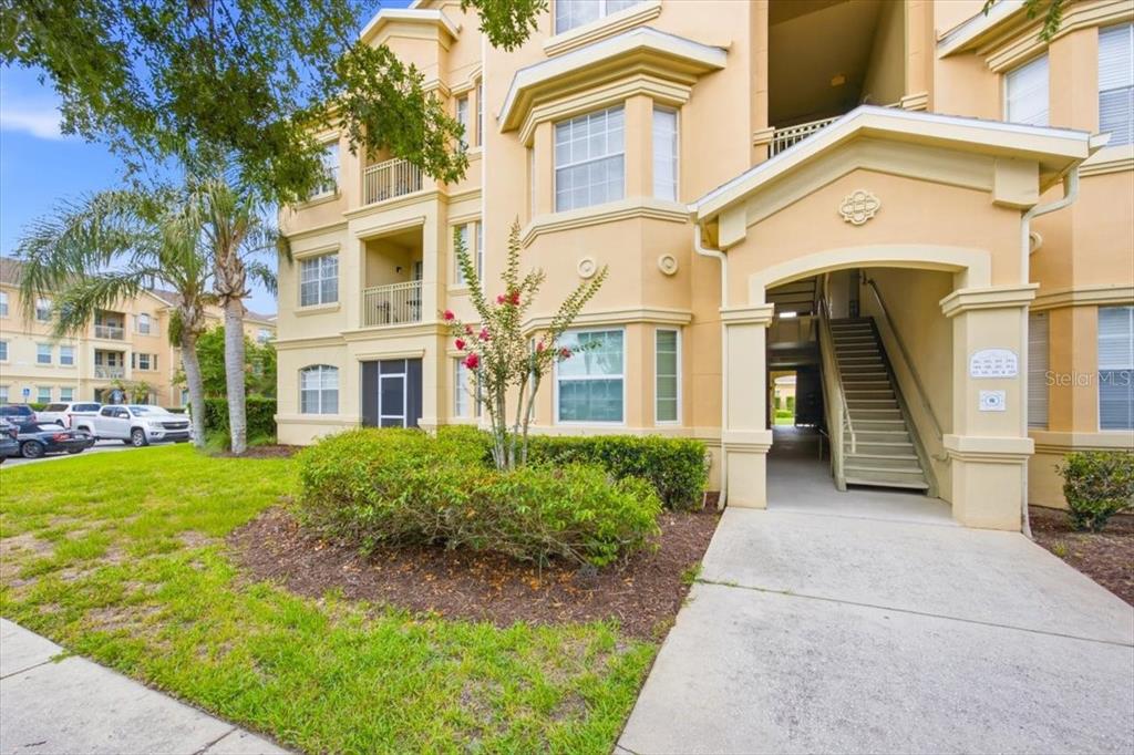 A multi-story tan apartment building features a covered entryway with stairs and a small garden — 301 TERRACE RIDGE CIRCLE UNIT 301, DAVENPORT, FL