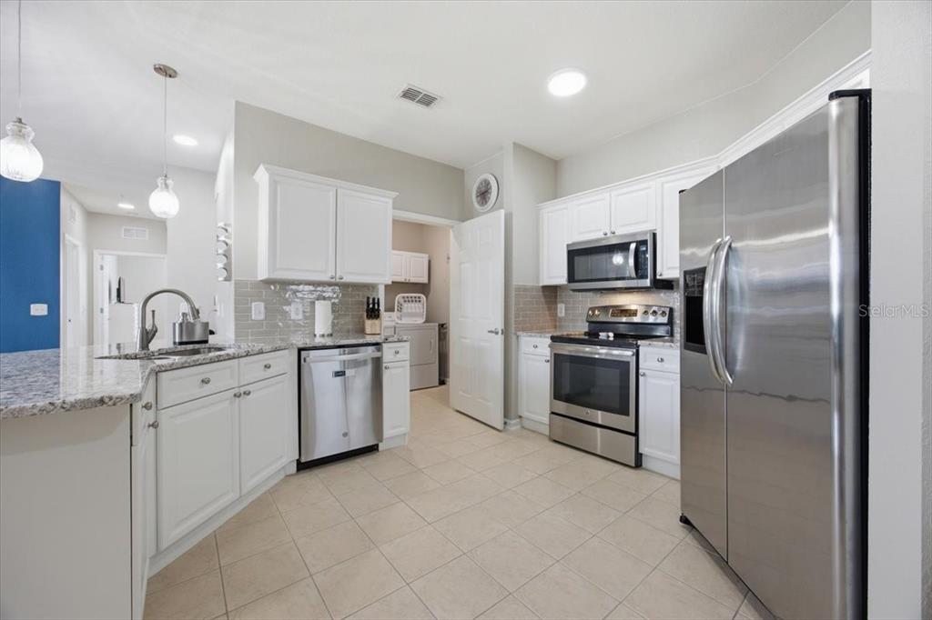 A kitchen features white cabinets, stainless steel appliances, granite countertops, and light-colored tile flooring — 301 TERRACE RIDGE CIRCLE UNIT 301, DAVENPORT, FL