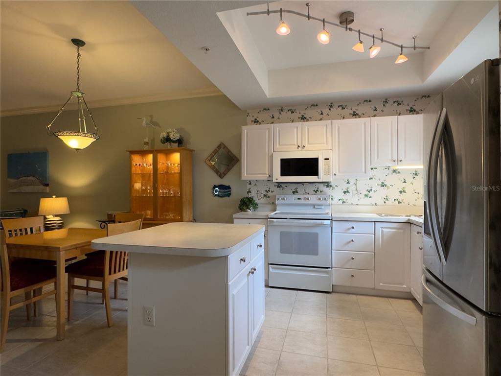 A kitchen features white cabinetry, a central island, stainless steel appliances, and floral wallpaper — 8370 WINGATE DRIVE UNIT 717, SARASOTA, FL
