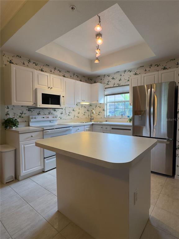 A kitchen with white cabinets, stainless steel appliances, a center island, and floral wallpaper — 8370 WINGATE DRIVE UNIT 717, SARASOTA, FL