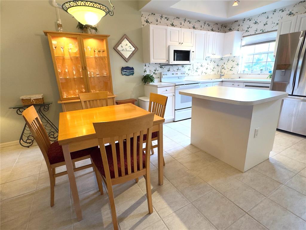 A kitchen features white cabinetry, a central island, and an adjacent dining area with chairs — 8370 WINGATE DRIVE UNIT 717, SARASOTA, FL