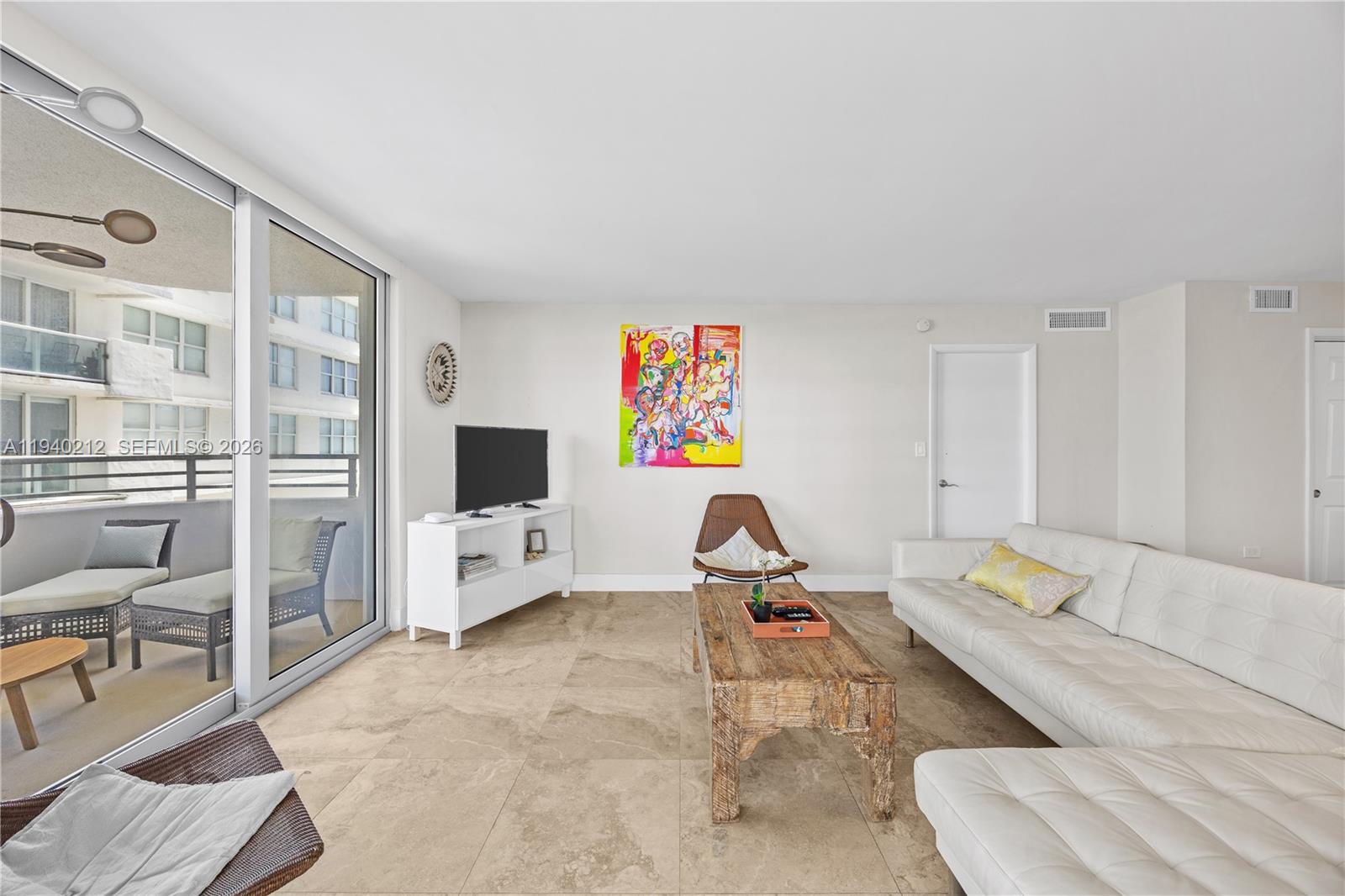 A living room features a white sofa, wooden coffee table, and a balcony with outdoor furniture — 5555 Collins Ave # 4B, Miami Beach FL 33140, MIAMI BEACH, FL
