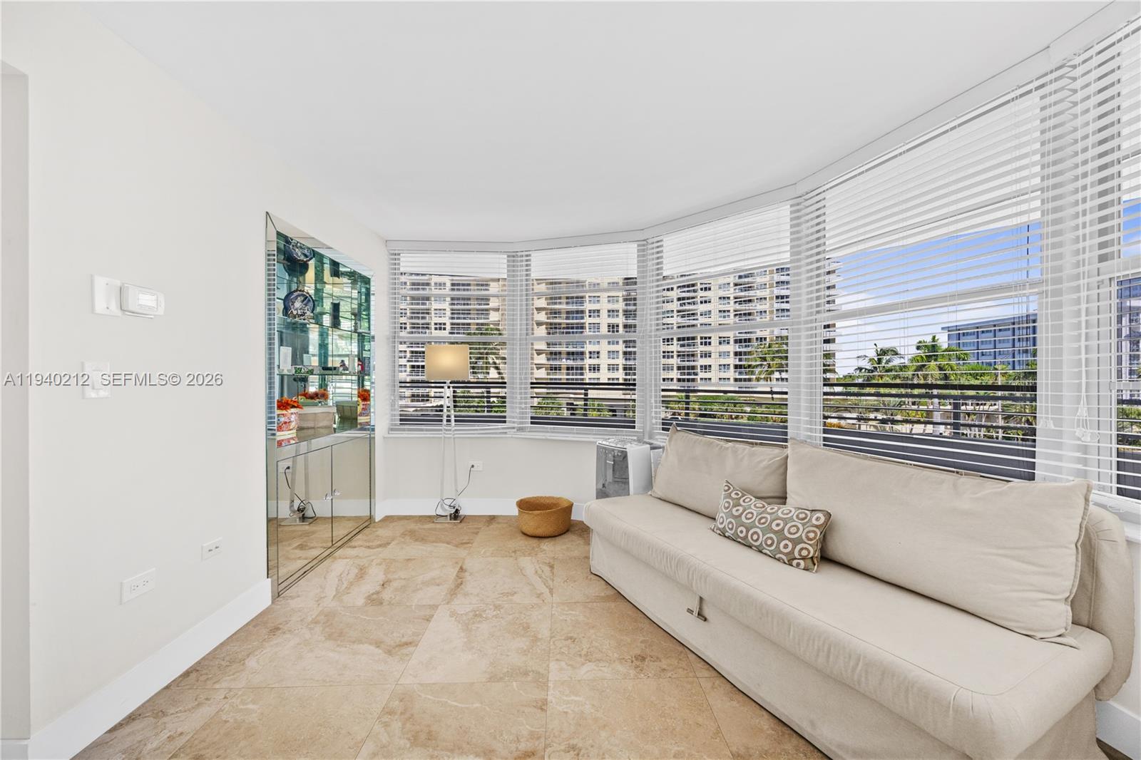 A living room features beige tile floors, a beige sofa, and large windows with blinds — 5555 Collins Ave # 4B, Miami Beach FL 33140, MIAMI BEACH, FL