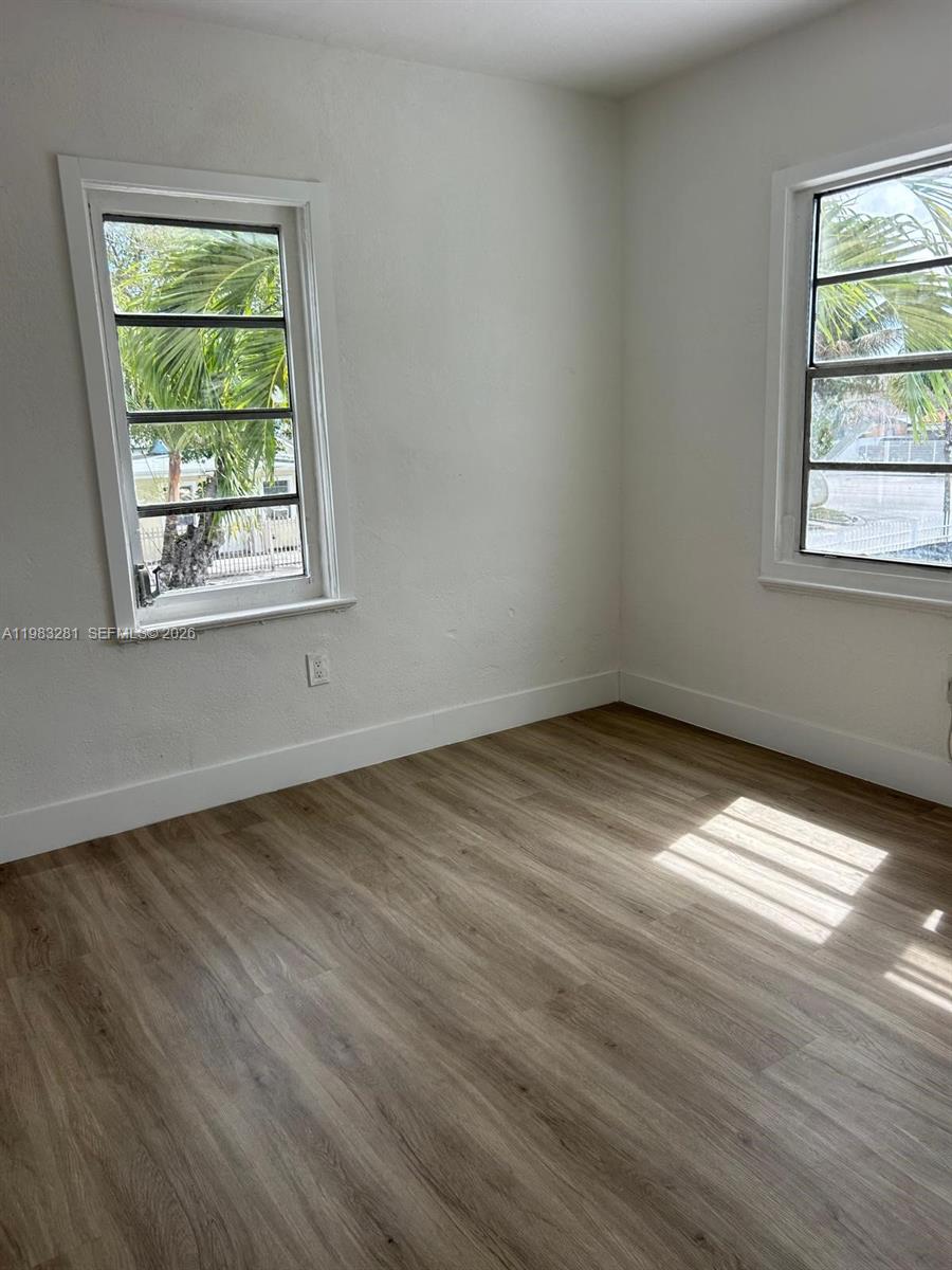 An empty room features light wood-look flooring, white walls, and two windows with exterior palm trees — 2908 NW 14 ct # 1, Miami FL 33142, MIAMI, FL