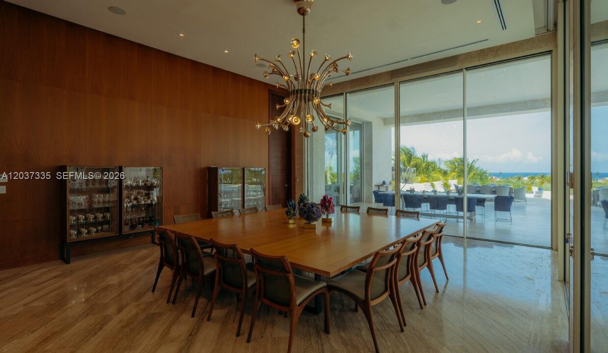 A dining room features a large square table, modern chandelier, wood paneling, and ocean views — 0 Fundadores de golf, FL, FL
