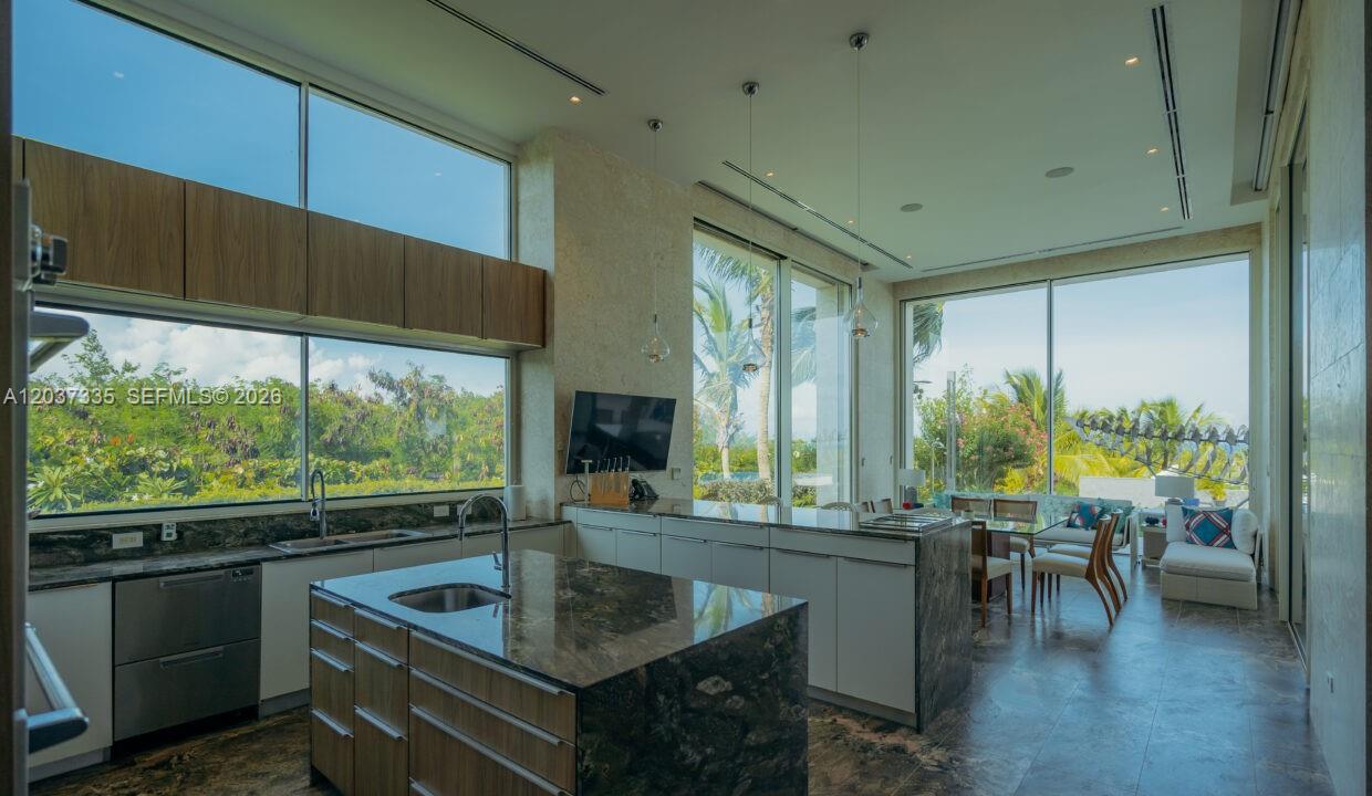 A modern kitchen with a dark stone island and floor-to-ceiling windows overlooking tropical greenery — 0 Fundadores de golf, FL, FL