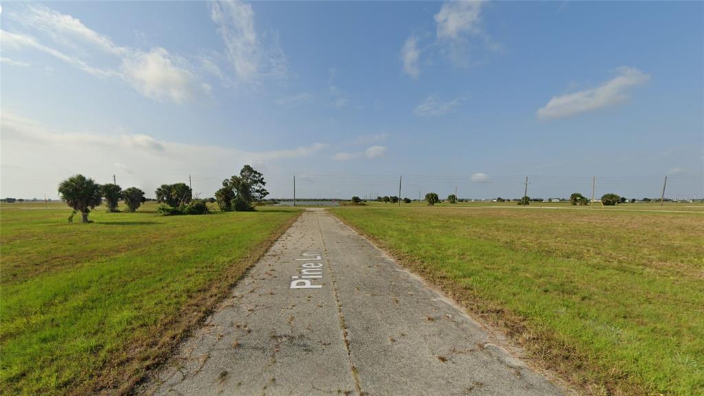 A paved road leads through a flat, grassy field under a blue sky with clouds — 10 PINE LANE, PLACIDA, FL