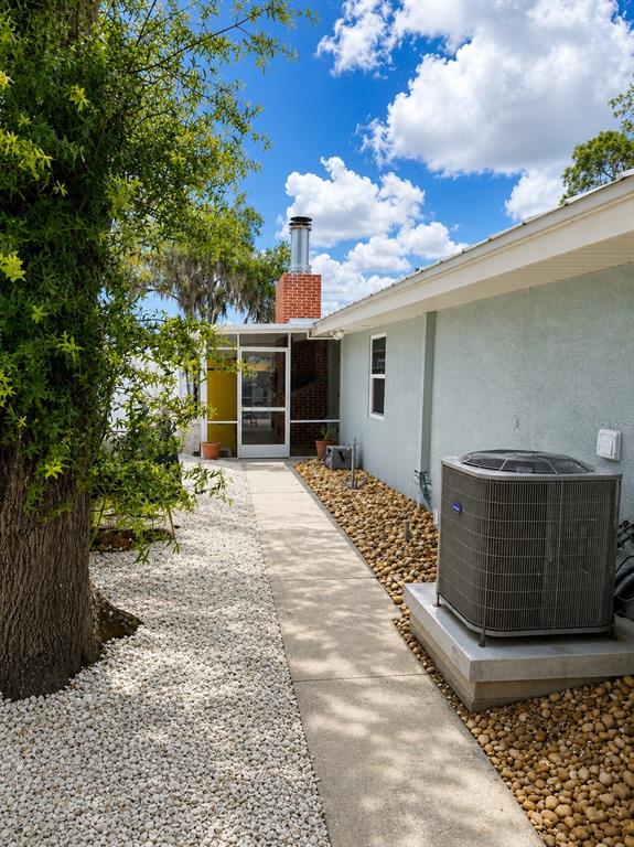 A concrete walkway leads past a house exterior with a brick chimney and AC unit — 5431 FOLEY SQUARE, NEW PORT RICHEY, FL