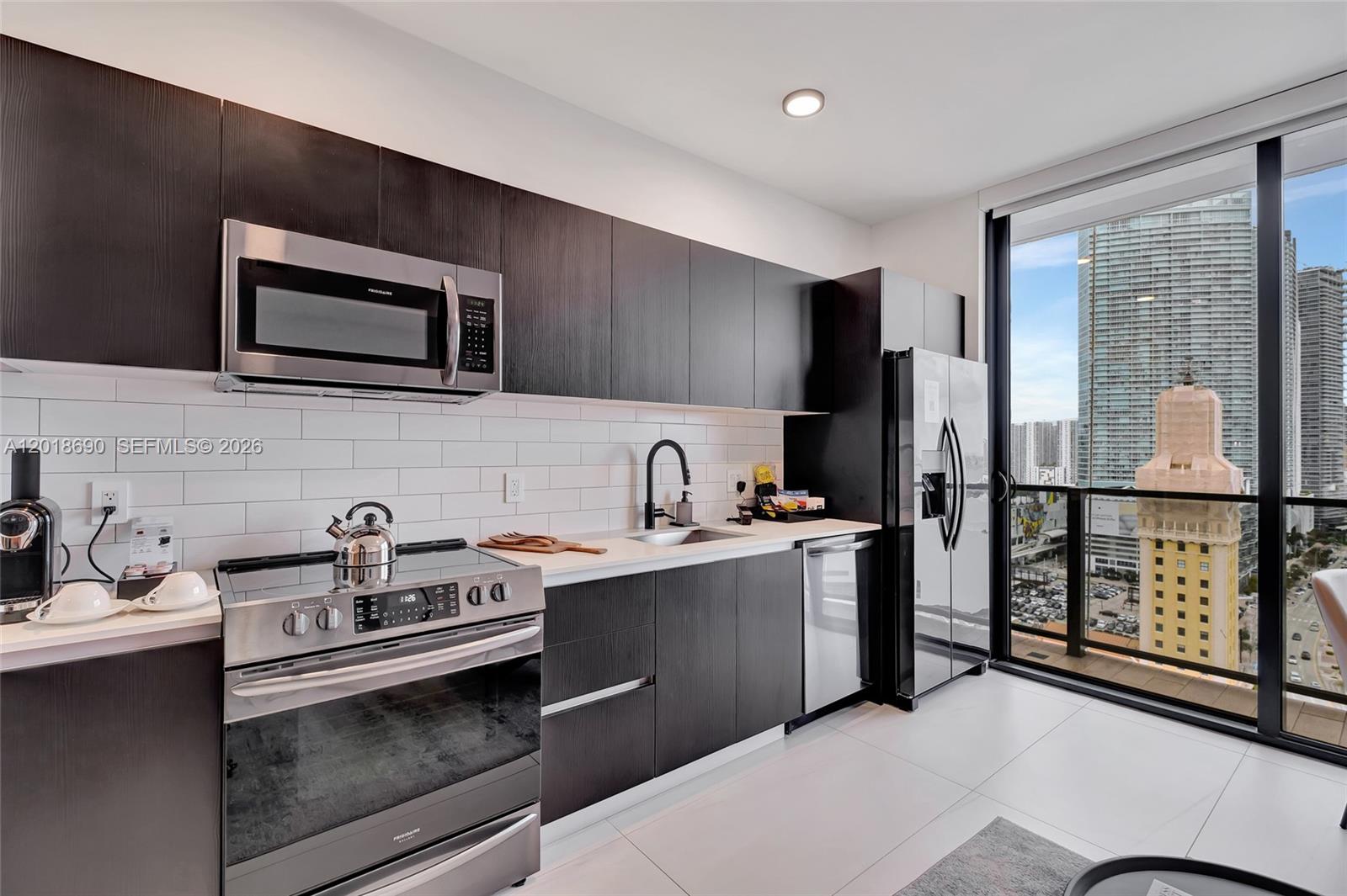 A modern kitchen features dark wood cabinetry, stainless steel appliances, and a view of skyscrapers — 398 NE 5th St # 1407, Miami FL 33132, MIAMI, FL