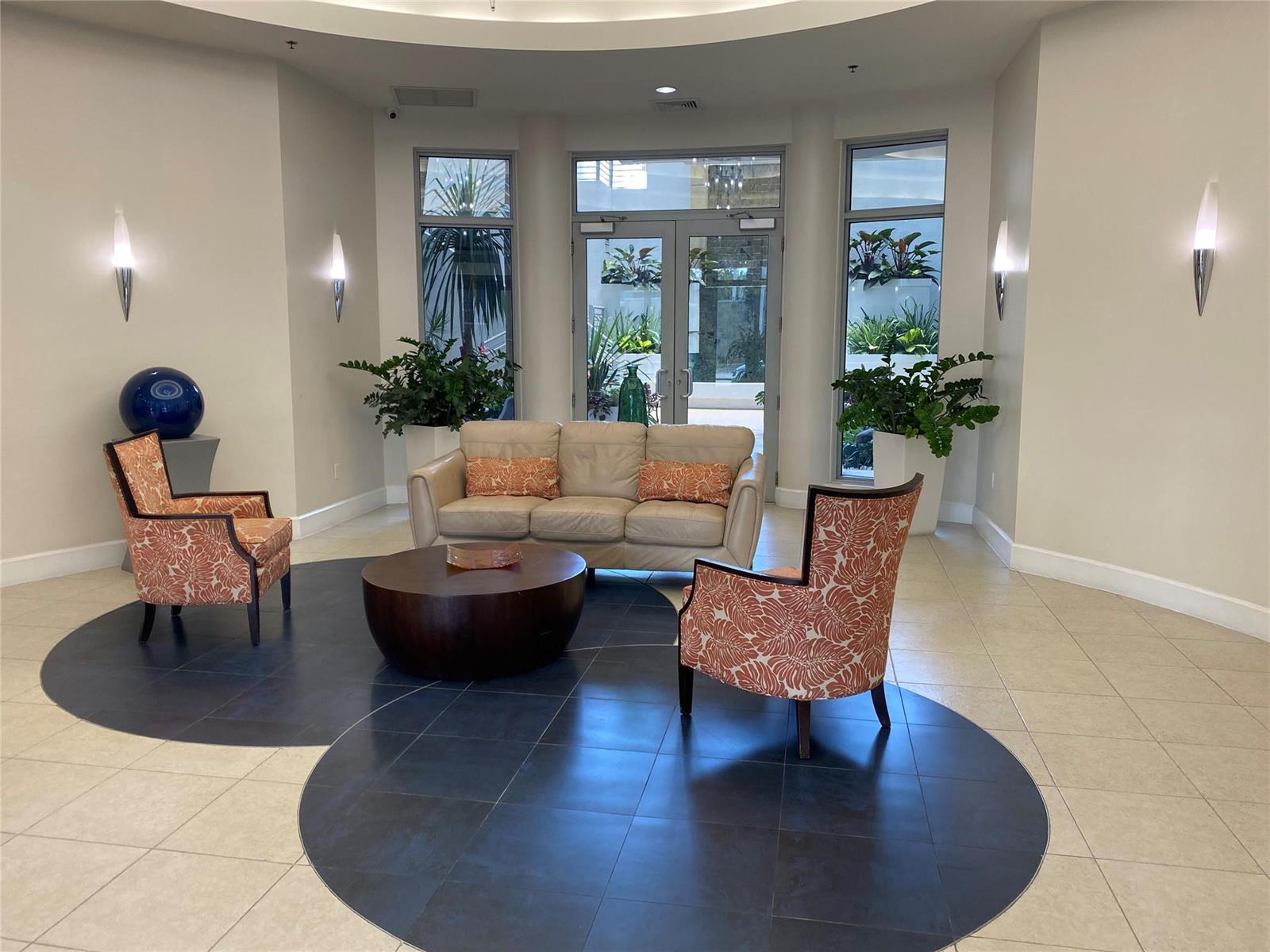 A lobby features a beige sofa, two patterned armchairs, and a circular dark tile floor — 1830 Radius Drive, Hollywood FL 33020, HOLLYWOOD, FL