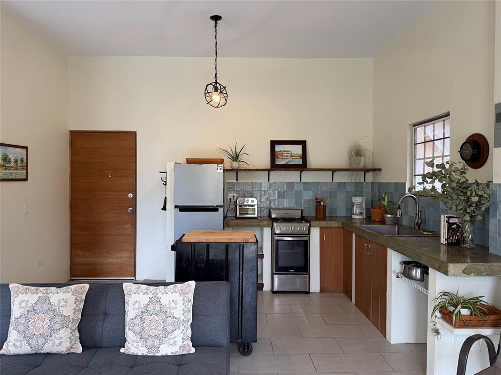 A kitchen with a stainless steel stove, refrigerator, wooden cabinets, and a gray sofa — 311 VILLA BORINQUEN, VIEQUES, PR