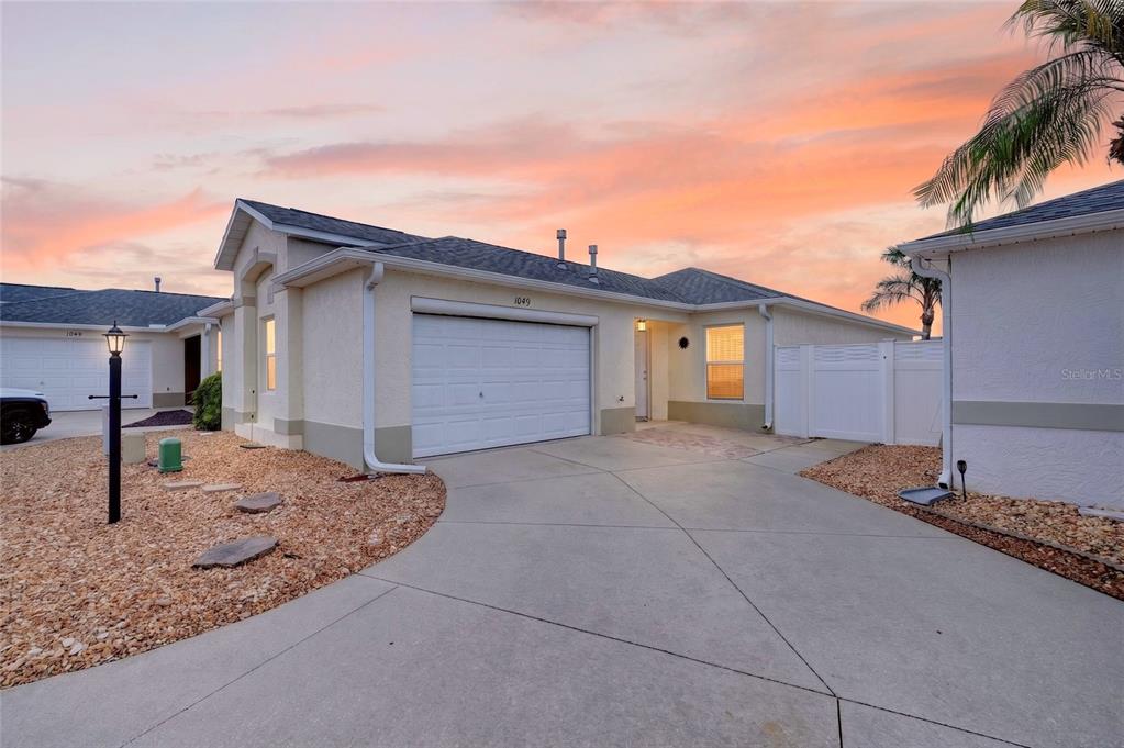 A single-story house with a white garage, beige stucco exterior, and a concrete driveway at sunset — 1049 JACKSON STREET, THE VILLAGES, FL