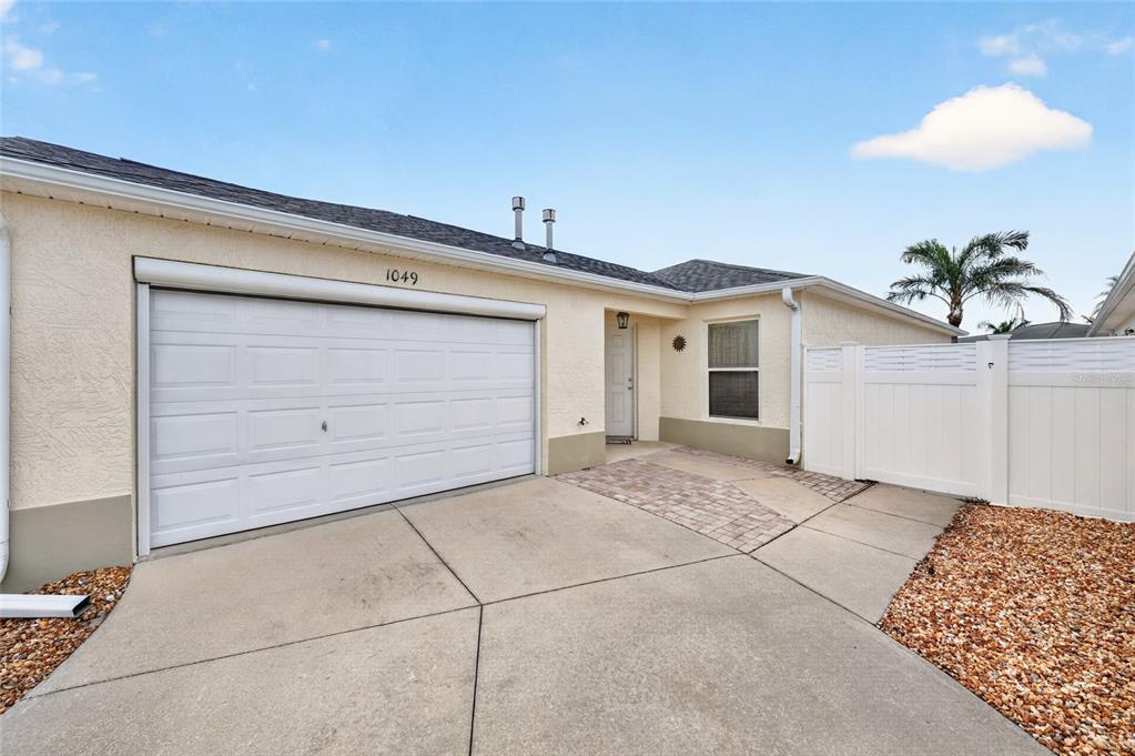 A single-story house exterior features a white garage door, a paved walkway, and a white fence — 1049 JACKSON STREET, THE VILLAGES, FL