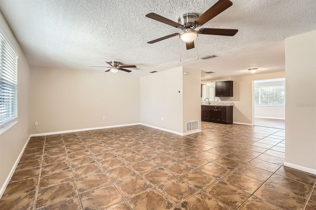 An open-concept living area with brown tile flooring, two ceiling fans, and a kitchen visible — 5023 THAMES DRIVE, NEW PORT RICHEY, FL