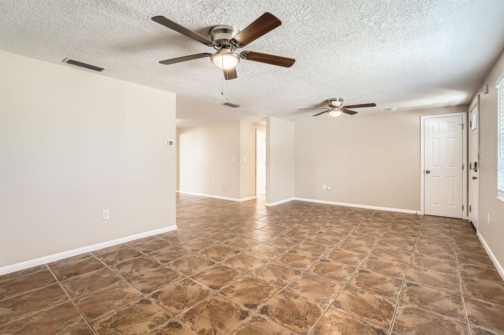 An open living area features tan walls, brown tiled floors, and two ceiling fans — 5023 THAMES DRIVE, NEW PORT RICHEY, FL