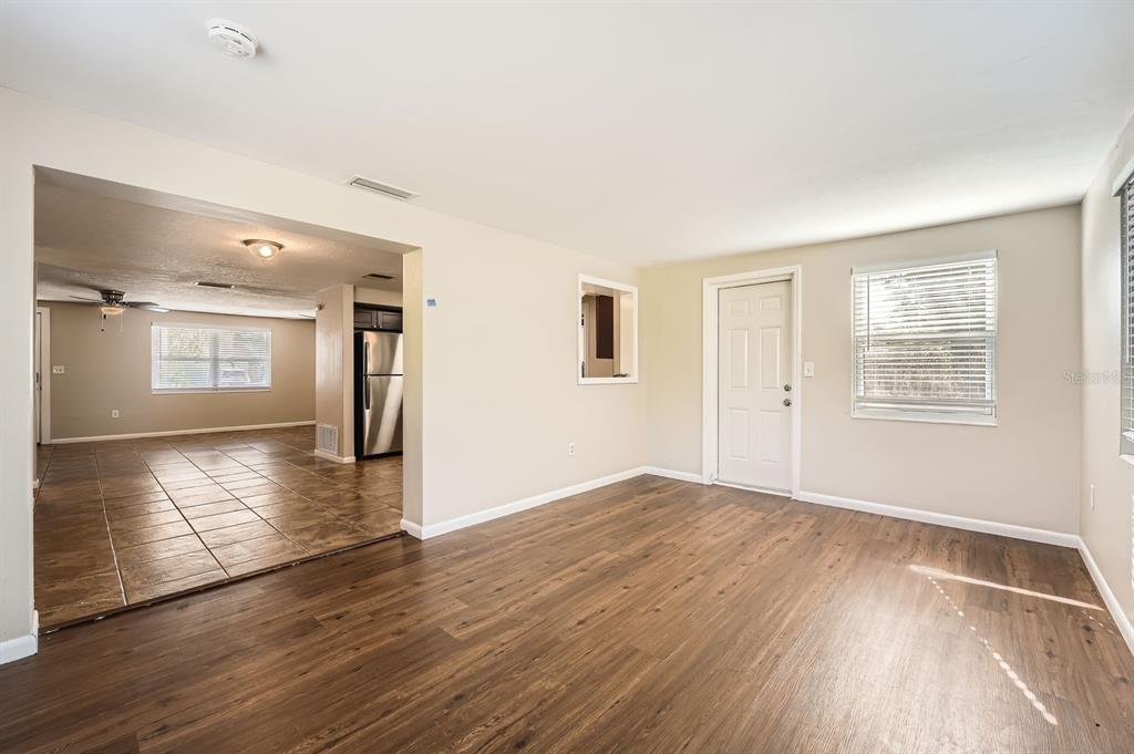 An interior view shows a living room with wood-look flooring leading to a tiled kitchen — 5023 THAMES DRIVE, NEW PORT RICHEY, FL