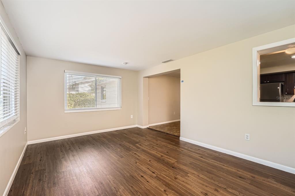 An empty room with wood-look flooring, beige walls, a window with blinds, and a pass-through — 5023 THAMES DRIVE, NEW PORT RICHEY, FL