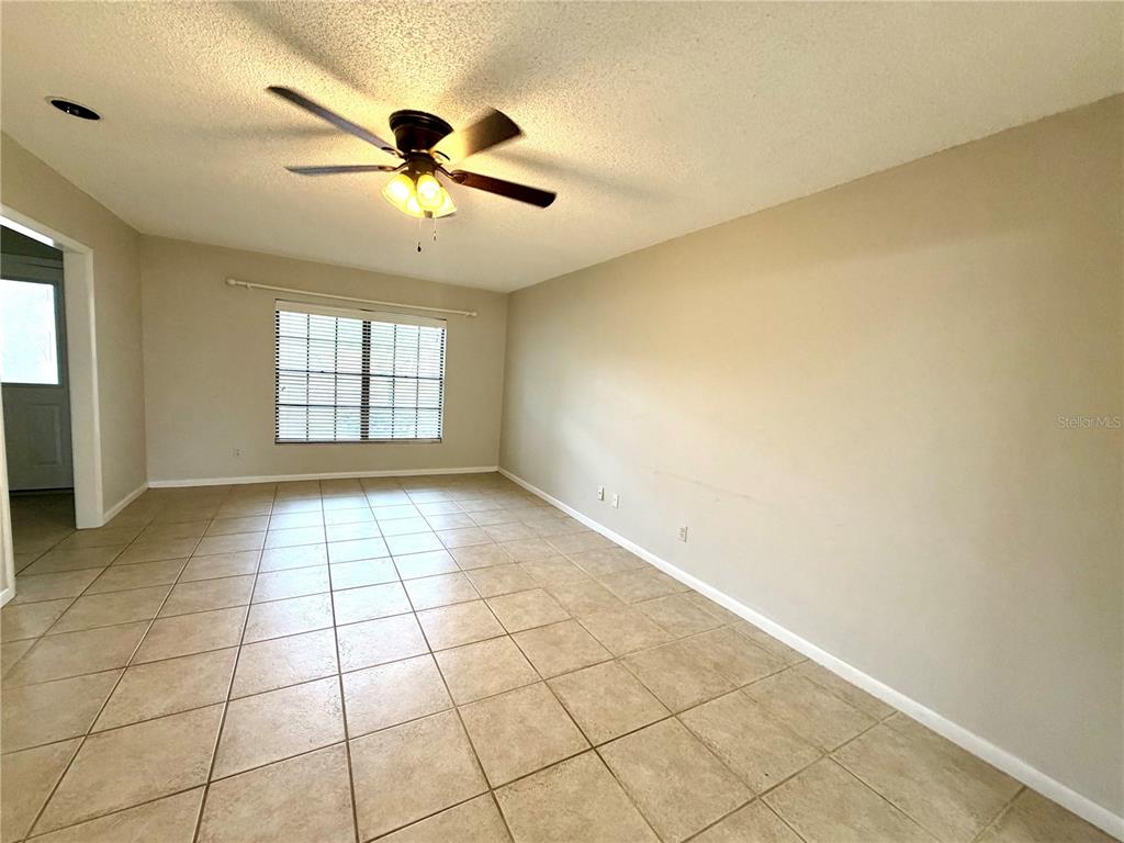 An empty room features beige walls, light-colored tile flooring, and a ceiling fan — 14904 LAKE FOREST DRIVE, LUTZ, FL