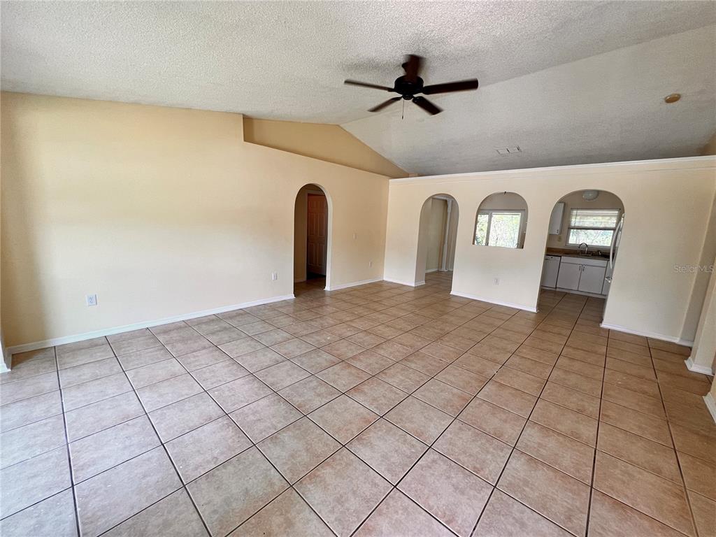 An open living area with tan tile flooring, a vaulted ceiling, and arched doorways — 390 FORT SMITH BOULEVARD, DELTONA, FL