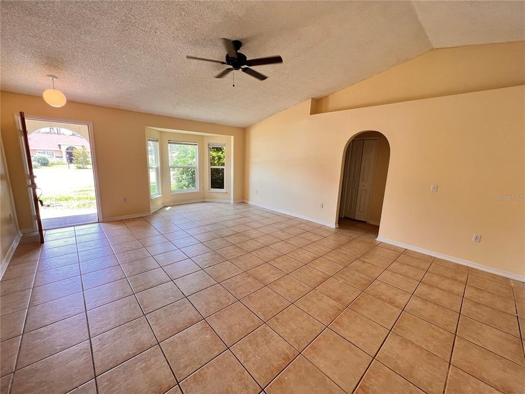An empty living room features tan tile flooring, a vaulted ceiling, and a bay window — 390 FORT SMITH BOULEVARD, DELTONA, FL
