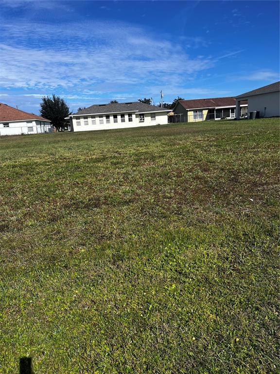 A grassy vacant lot sits in front of several residential houses under a blue sky — 725 LEONARDO COURT, KISSIMMEE, FL