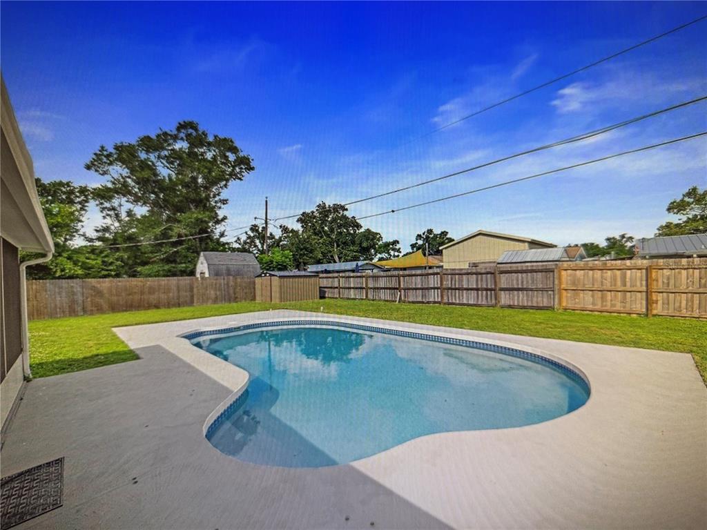 A backyard features a kidney-shaped swimming pool surrounded by a concrete patio and wooden fence — 3032 GOLDEN RAIN DRIVE, SARASOTA, FL