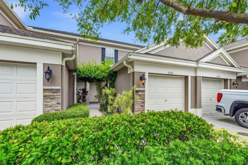 The exterior of a multi-unit townhouse complex features beige stucco walls, stone accents, and garages — 11221 WINDSOR PLACE CIRCLE, TAMPA, FL