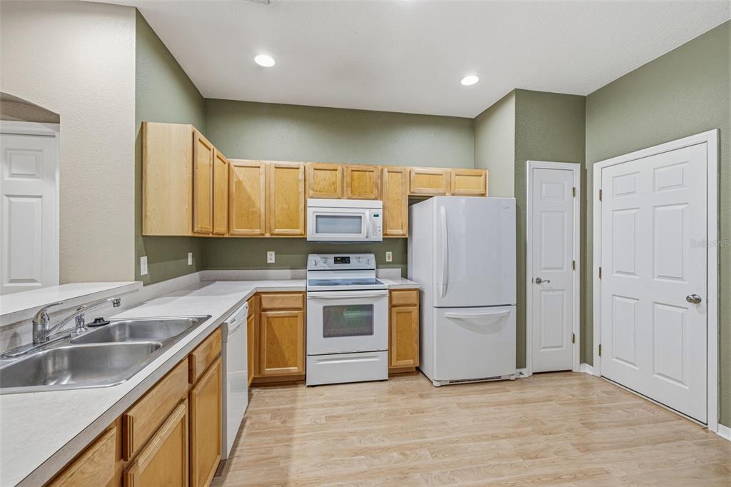 A kitchen features light wood cabinets, white appliances, laminate countertops, and olive green walls — 11221 WINDSOR PLACE CIRCLE, TAMPA, FL