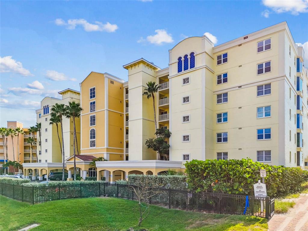 A multi-story yellow apartment building stands behind a black metal fence and green lawn — 16750 GULF BOULEVARD UNIT 315-A, NORTH REDINGTON BEACH, FL