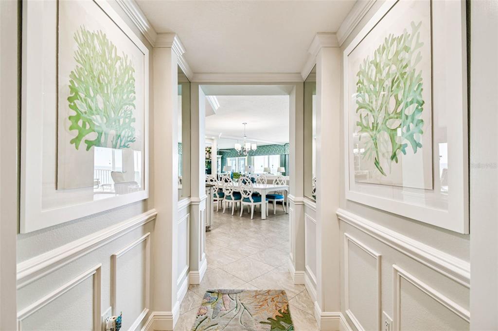 A hallway with wainscoting and framed coral art leads into a dining room — 16750 GULF BOULEVARD UNIT 315-A, NORTH REDINGTON BEACH, FL