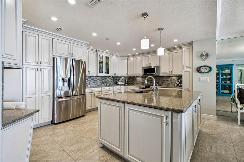 A kitchen features white cabinetry, granite countertops, a stainless steel refrigerator, and a central island — 16750 GULF BOULEVARD UNIT 315-A, NORTH REDINGTON BEACH, FL